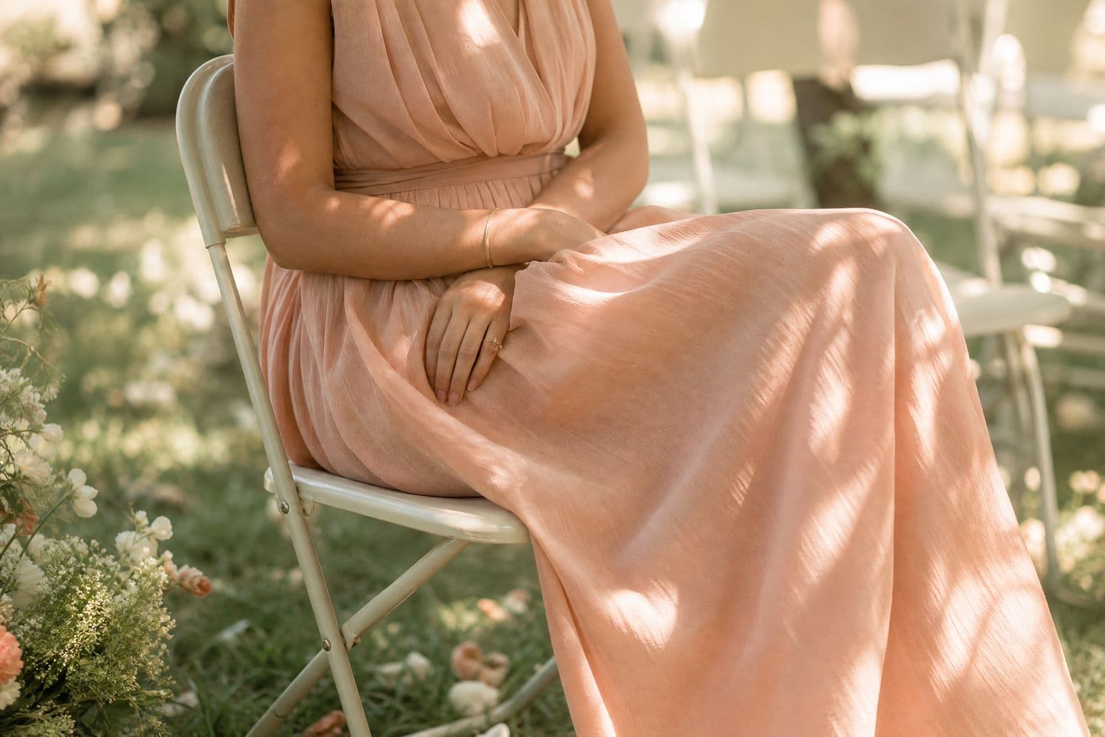 A seated figure at an outdoor garden ceremony photographed from the chest down, with the dress hem gathered across the lap.